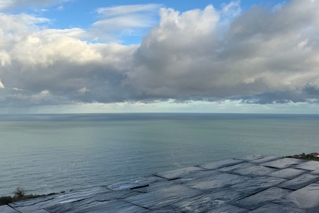 Rain-soaked moiré phyllite facade with stormy Cantabrian Sea horizon at dawn, Akelarre Hotel