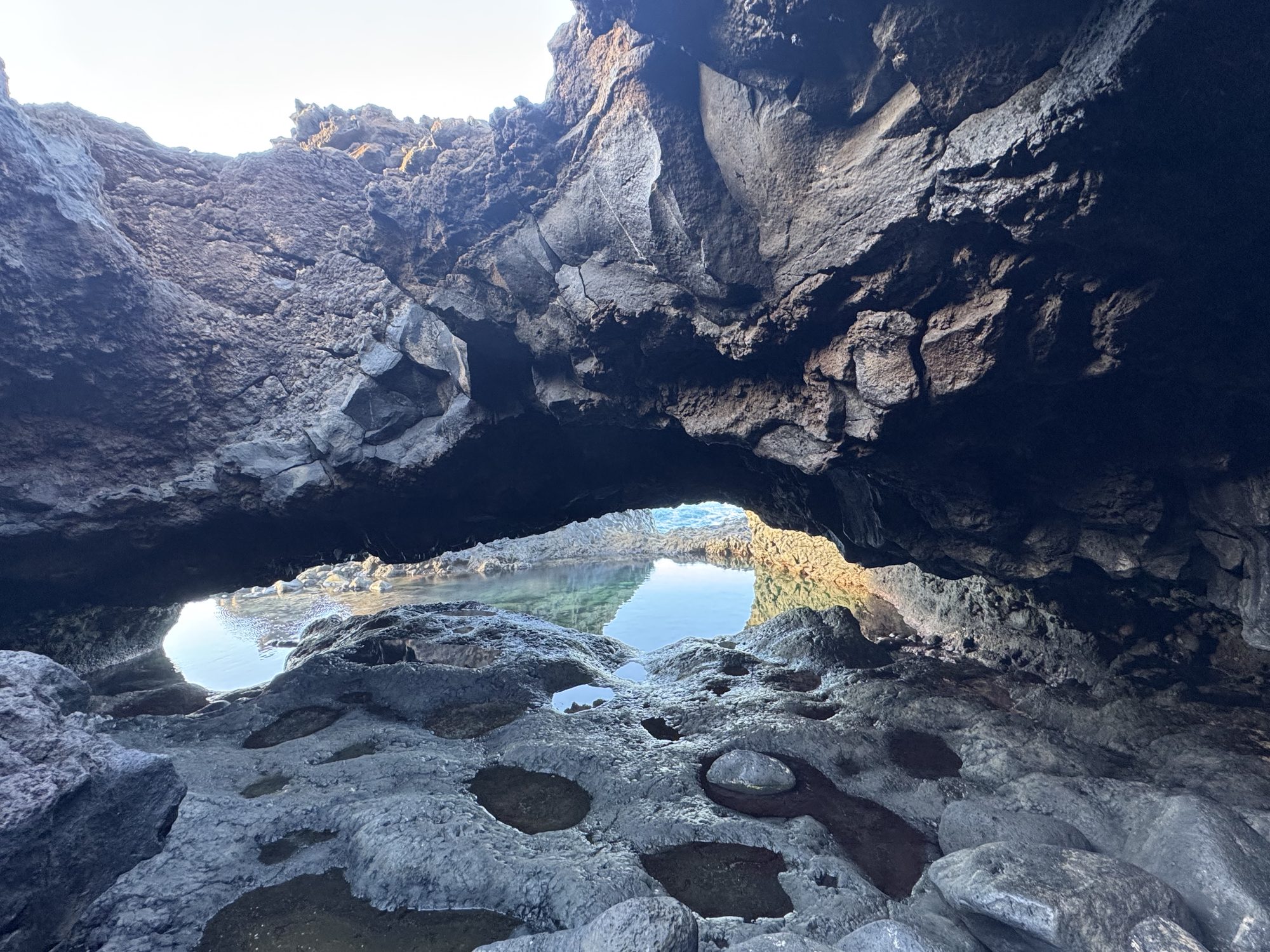 Turquoise natural pool enclosed by black lava rock under a lava arch, El Hierro