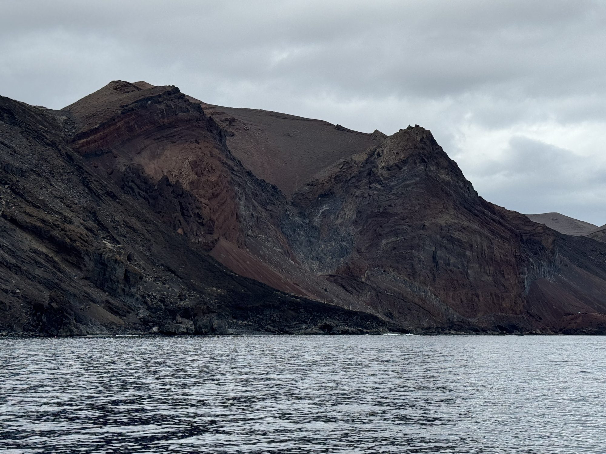 Layered red and ochre volcanic cliffs seen from a boat, El Hierro